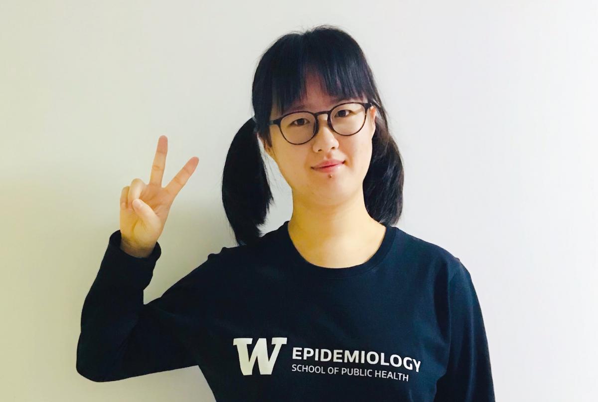 Shengruo is wearing a UW Epidemiology shirt and holds up peace sign.