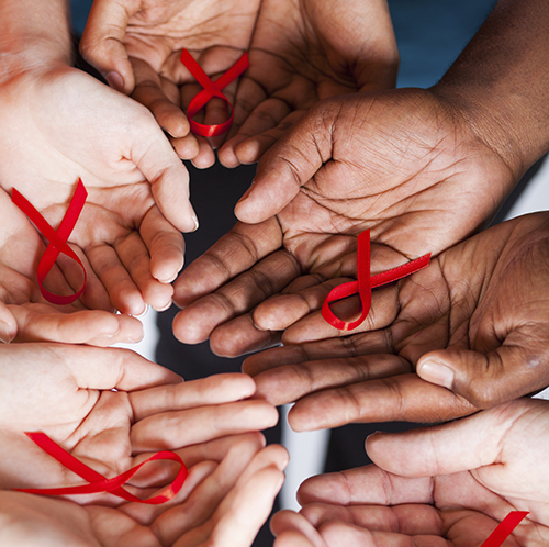 A group of hands holding red bows signifying HIV/AIDS awareness